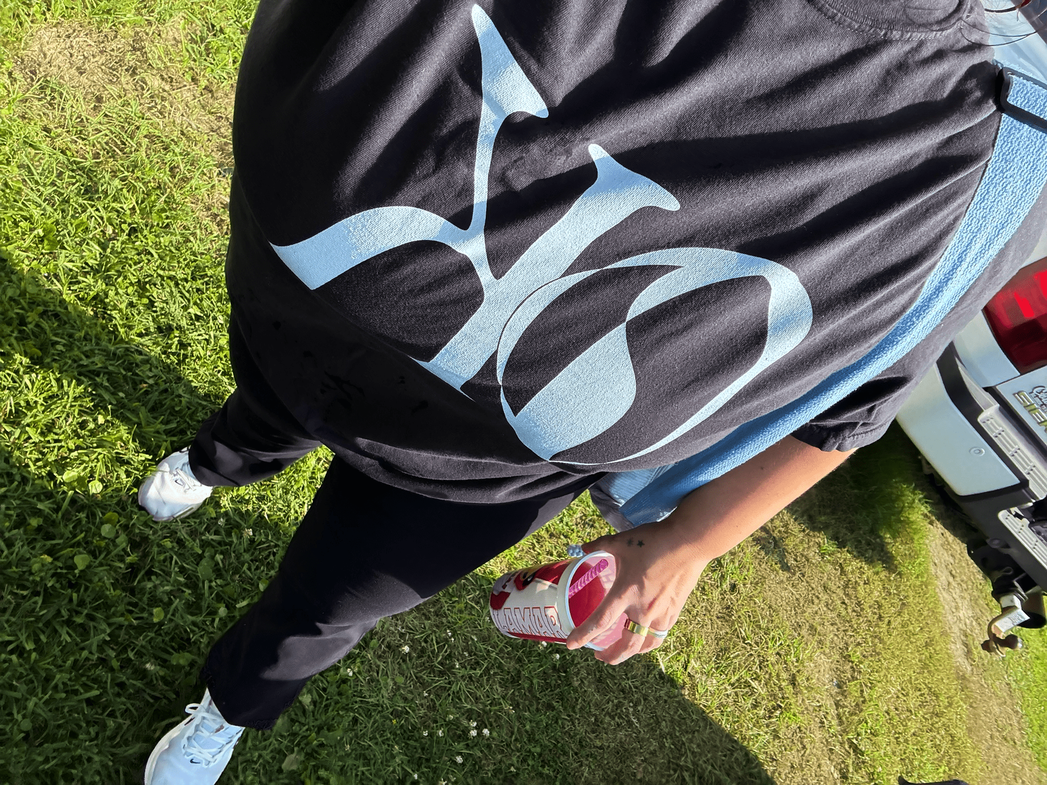 KO Creative Agency Logo Tee with only KO. On Kaitlin on a black tee with light blue letters. Kaitlin is outside and carrying a drink.